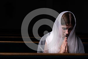 A young modest girl with a handkerchief on her head is sitting in church and praying. The concept of religion, prayer, worship