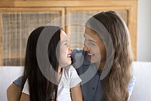 Young mom and cute little daughter hugging seated on sofa