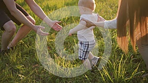 Young mom, dad teaches infant child to walk on grass in green park.