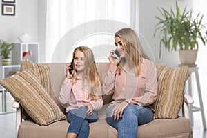 Young mom and daughter  spend time together at home. They are sit on the couch  having fun talking on the phone