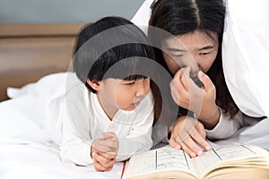 Young mom and daughter telling storybook in bed