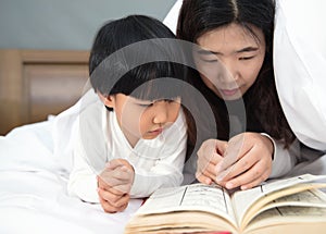 Young mom and daughter telling storybook in bed