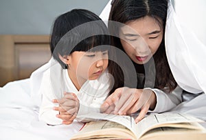 Young mom and daughter telling storybook in bed