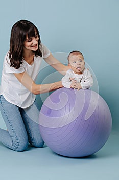 Young mom doing gymnastics with a baby on a lilac fitness ball