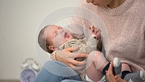 Young mom feeding little baby son from bottle, infant formula artificial feeding