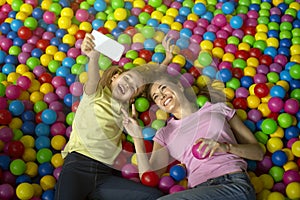 Young mom with her daughter taking selfie while playing in ball pond at indoor amusement park, above view