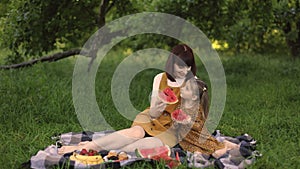 Young mom with her little cute daughter on a picnic in green park eating watermelon.