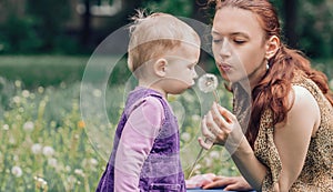 Young mom with her little daughter blowing on a dandelion