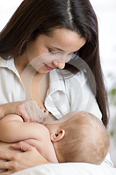 Young mother holding her newborn child. Mom nursing baby. Pretty woman breast feeding kid.