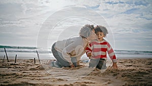 Young mom kissing child on weekend holidays. Happy parent building sand castle