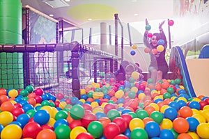 Young mom playing with kids in pool with colorful balls