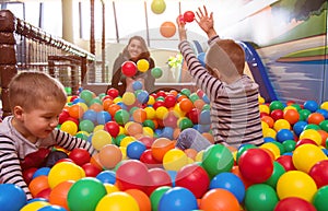 Young mom playing with kids in pool with colorful balls
