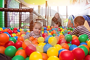 Young mom playing with kids in pool with colorful balls