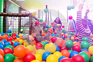 Young mom playing with kids in pool with colorful balls