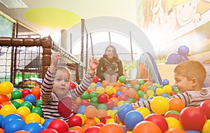 Young mom playing with kids in pool with colorful balls