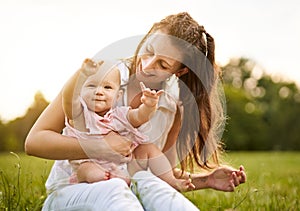 Young mom sitting in a park in the grass with his little baby daughter on her lap - 20s wife plays with his child while the baby