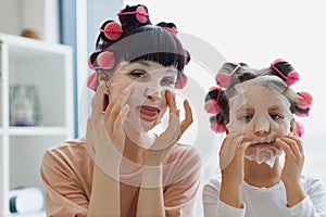 Young mom teaches her little cute daughter to take care of her face skin.