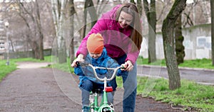 Young mom teaching son to ride bike first time in park. Happy kids on bikes