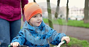 Young mom teaching son to ride bike first time in park. Happy kids on bikes