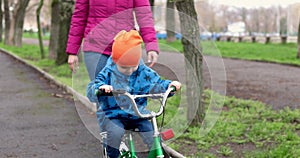 Young mom teaching son to ride bike first time in park. Happy kids on bikes