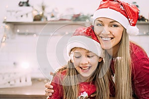 Young mom and teenage daughter in the kitchen in red hat laughing and faces are covered in flour.