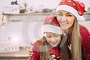 Young mom and teenage daughter in the kitchen in red hat laughing and faces are covered in flour