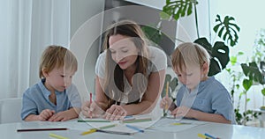 Young Mom and two sons 2-4 years old draw pencils drawing on boomega sitting at the living room table in slow motion