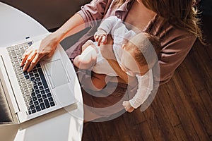 Young mom working remotely on laptop while taking care of her baby.