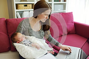 Young mom works remotely from home office with newborn baby. Freelancer woman holding her infant while using laptop. Workplace in