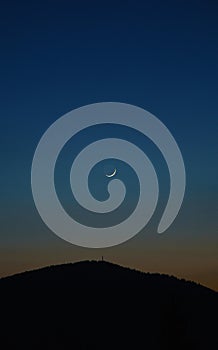 Young moon above mountain peak on blue sky