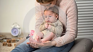 Young mother admiring sons tiny legs, baby sitting on womans lap, happiness