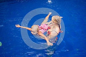 Young mother and adorable daughter having fun in pool. Learning