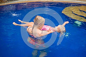 Young mother and adorable daughter having fun in pool. Learning