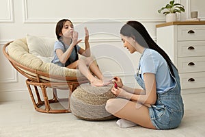 Young mother applying polish on daughter`s nails at home