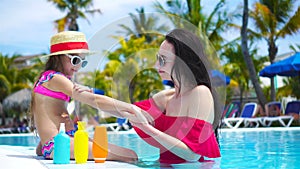 Young mother applying sun cream to kid nose in swimming pool. The concept of protection from ultraviolet radiation