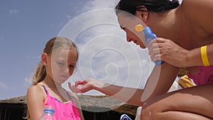 Young mother applying sunscreen lotion on face skin to daughter on beach