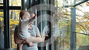 Young mother approaches window holding baby and smiling