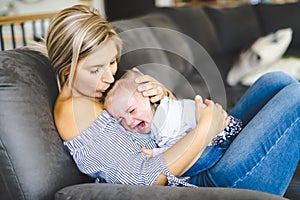 Young mother with baby daughter on sofa at home, the baby crying