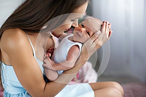 Young mother with baby in hands at home in the bedroom