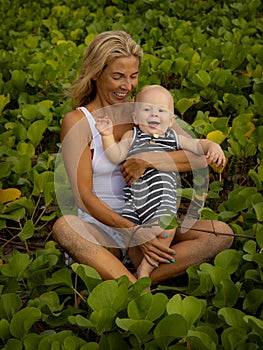 Young mother with baby infant boy spending time in nature. Outdoor activities. Mom and baby boy sitting on the ground. Smiling kid