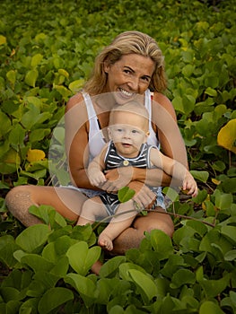 Young mother with baby infant boy spending time in nature. Outdoor activities. Mum and baby boy sitting on the ground. Happy