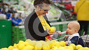 Young mother with baby shopping in supermarket. The child looks at lemon with delight, the development of kids