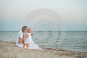 Young mother and baby sitting on sandy beach. Sea vacation with little children