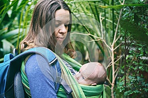 A young mother with a baby in a sling is walking in the jungle