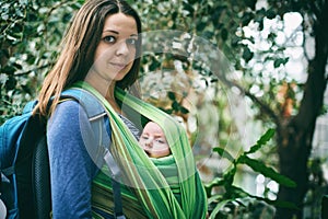 A young mother with a baby in a sling is walking in the jungle