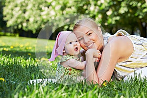 Young mother and baby snuggle their cheeks, sitting on grass