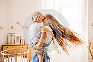 Young mother or babysitter with a little girl in her arms spin in the middle of the room