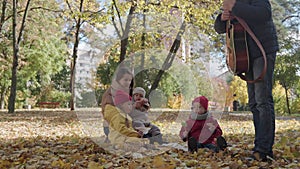 young mother babysitter walks in park picnicking with three small children sitting on blanket. Kids eat candy sweets