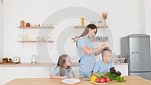 Young mother braids her son& x27;s hair while sitting in the kitchen. Children& x27;s breakfast