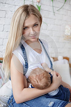 Young mother breastfeeding a child sitting on a bed in a bright bedroom